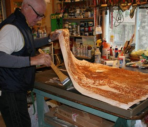 Bob Hainstock adhering rust print to plywood panel in printmaking process 